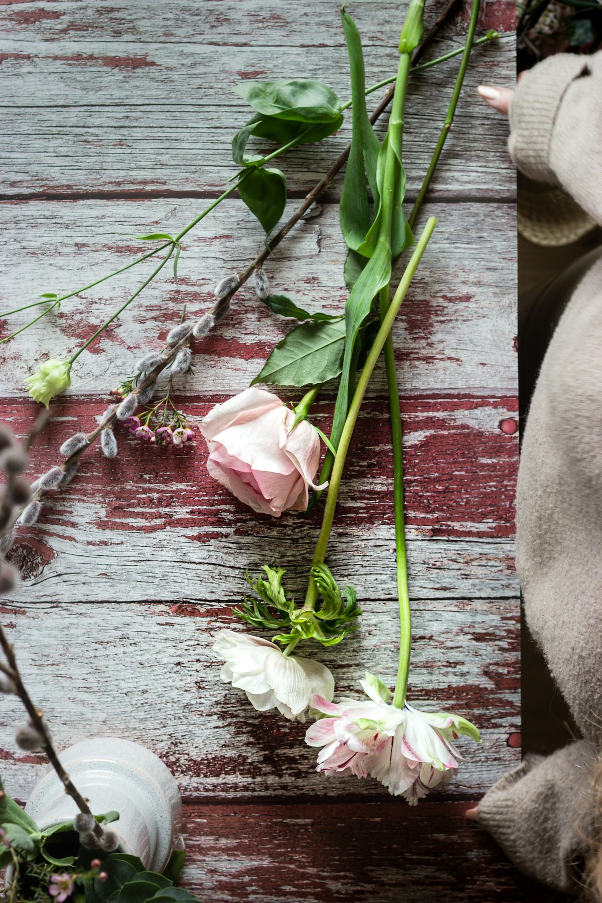 Hands arranging fresh stems on a worn wooden table